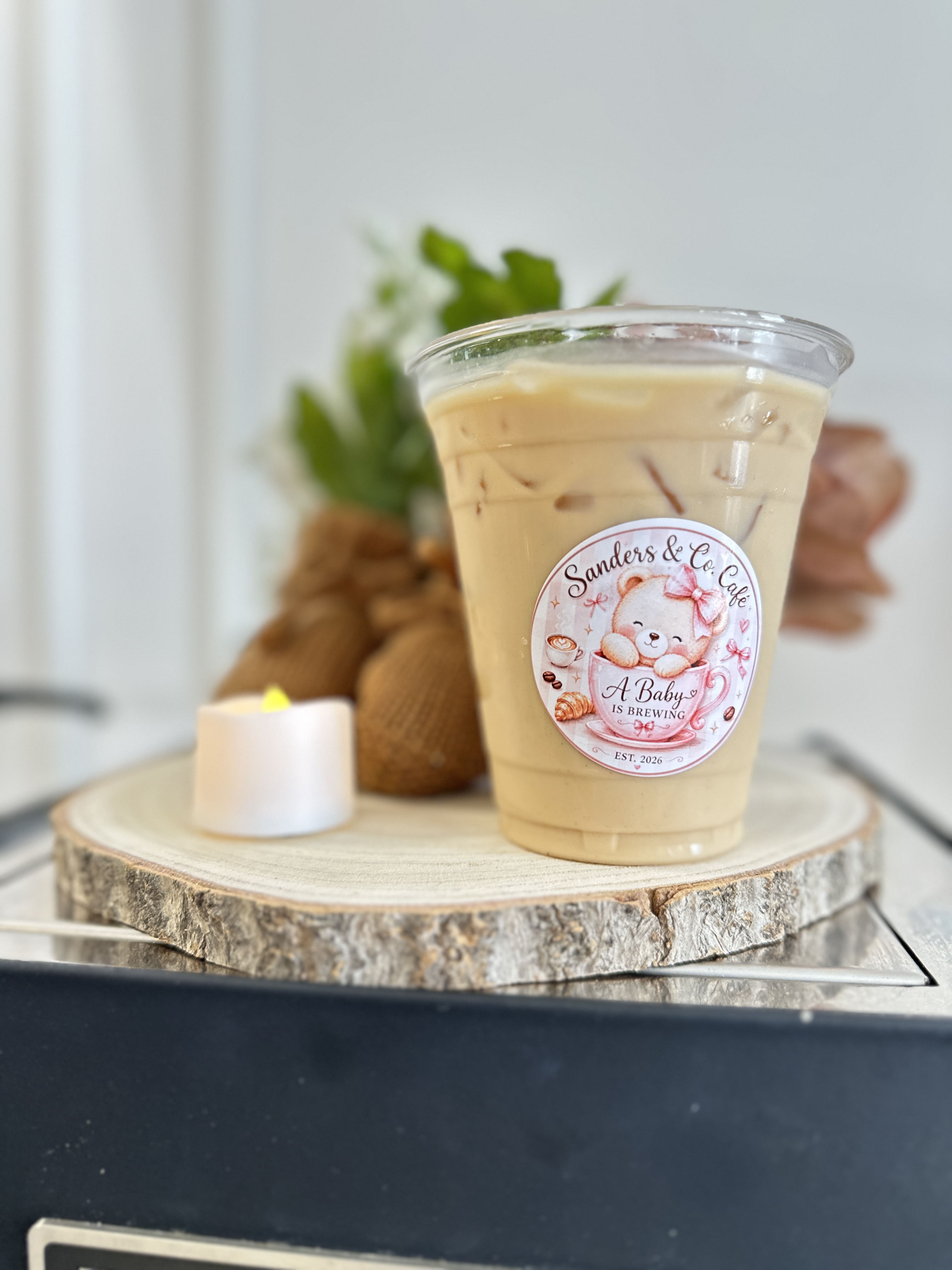 Tee Coffee Studio branded iced latte styled with white flowers and candle on wood slice at Atlanta baby shower