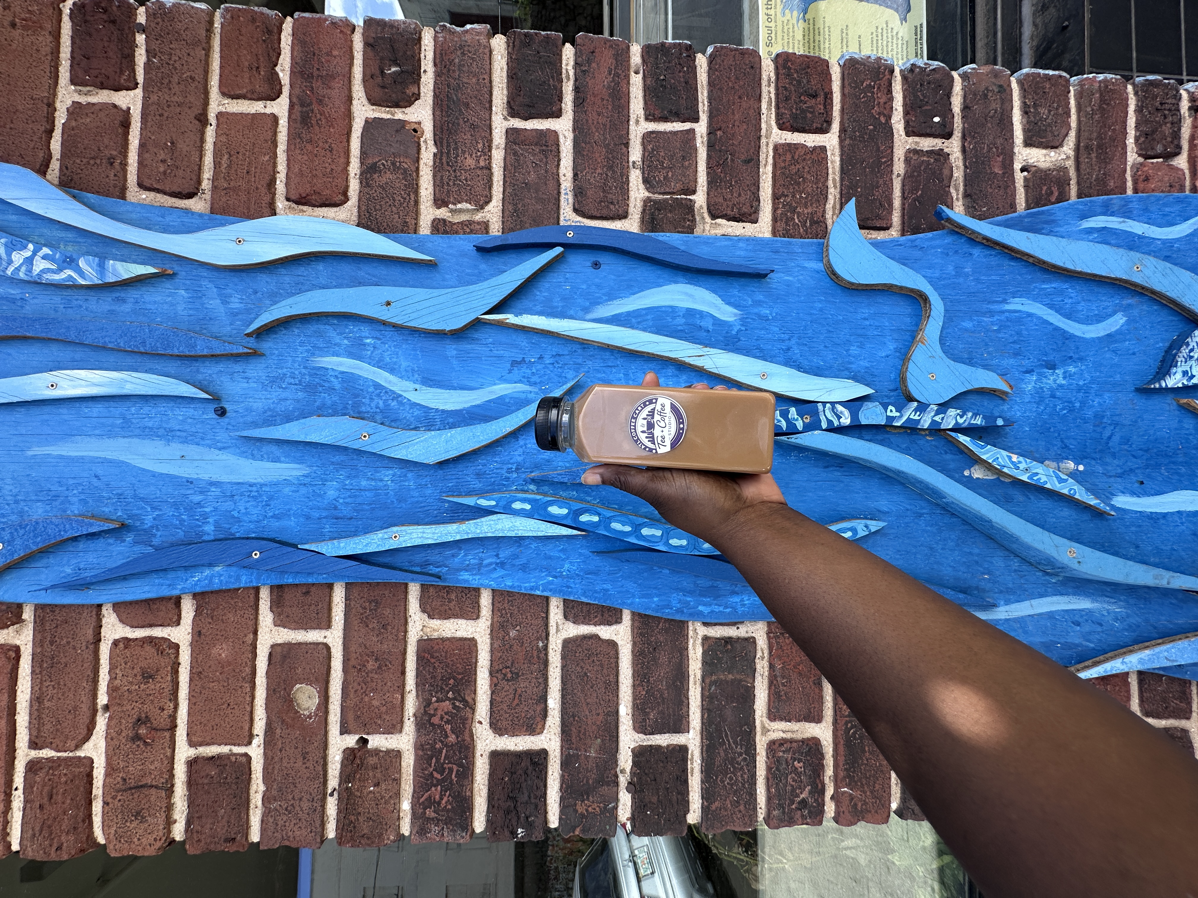 Tee Coffee Studio branded bottled latte held in front of blue Atlanta street art mural