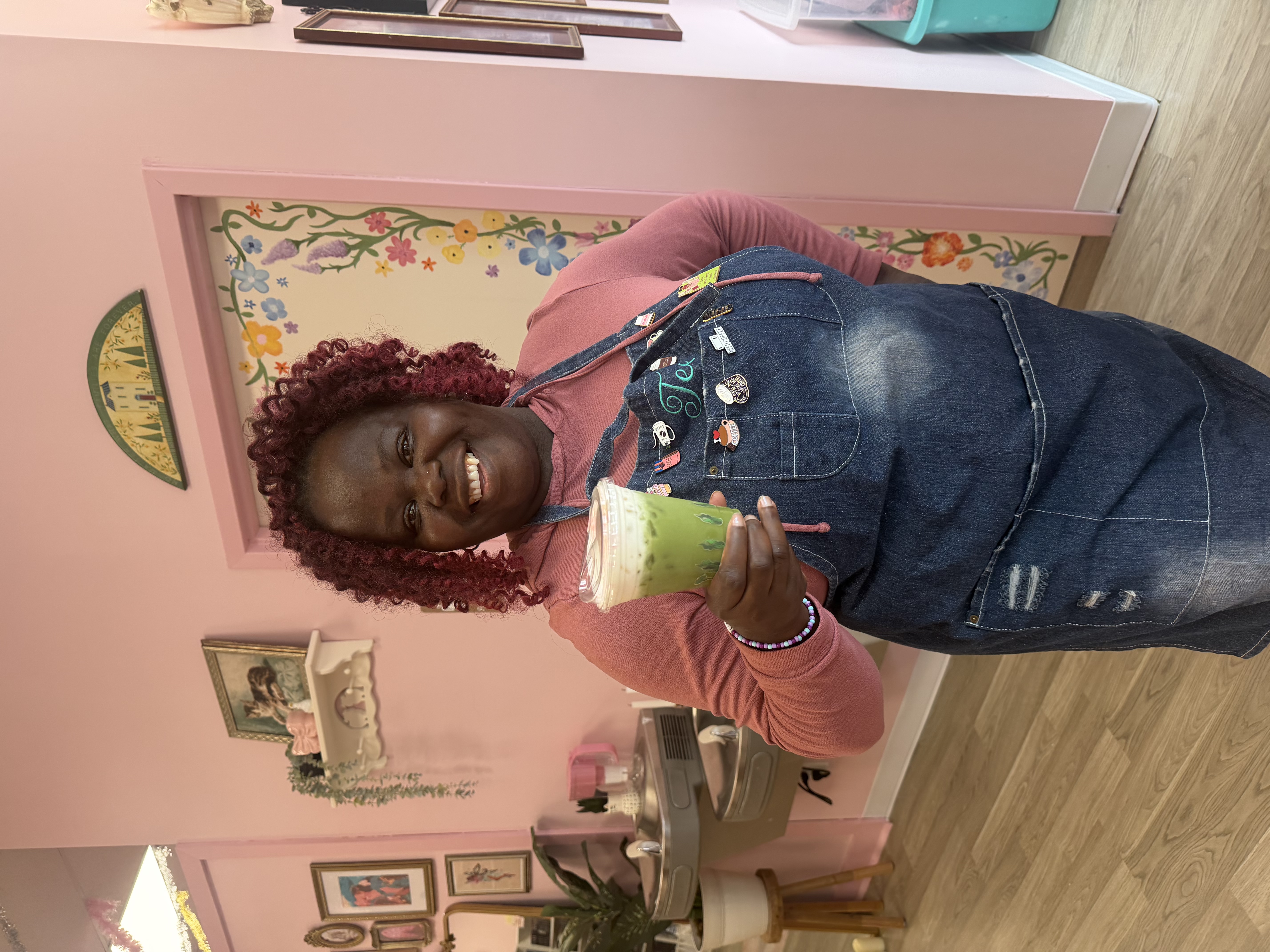 Tee George holding iced matcha latte at Atlanta community bookstore event wearing denim apron