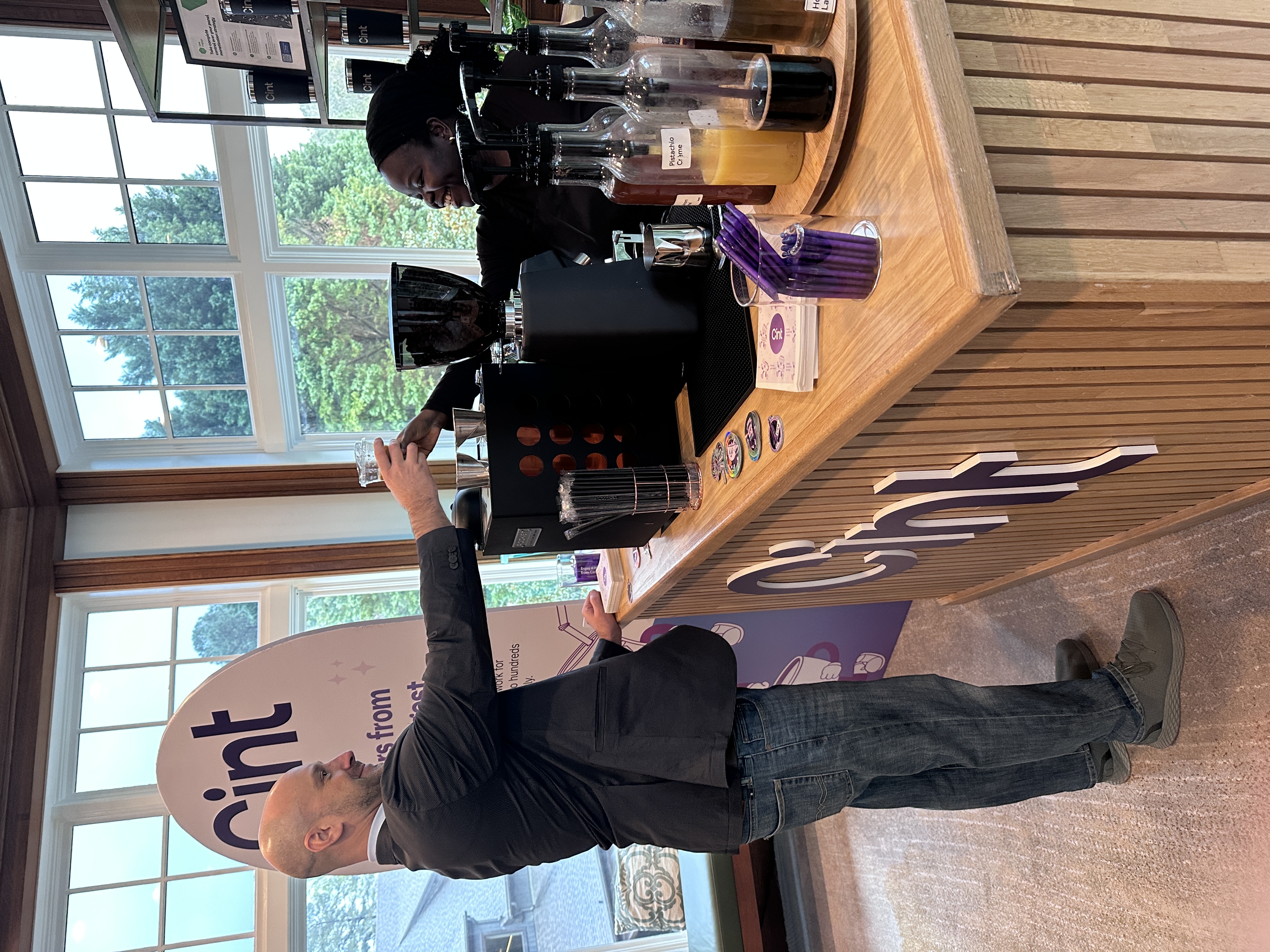 Tee George handing a specialty drink across the bar to a smiling guest at Atlanta corporate conference — the moment of service