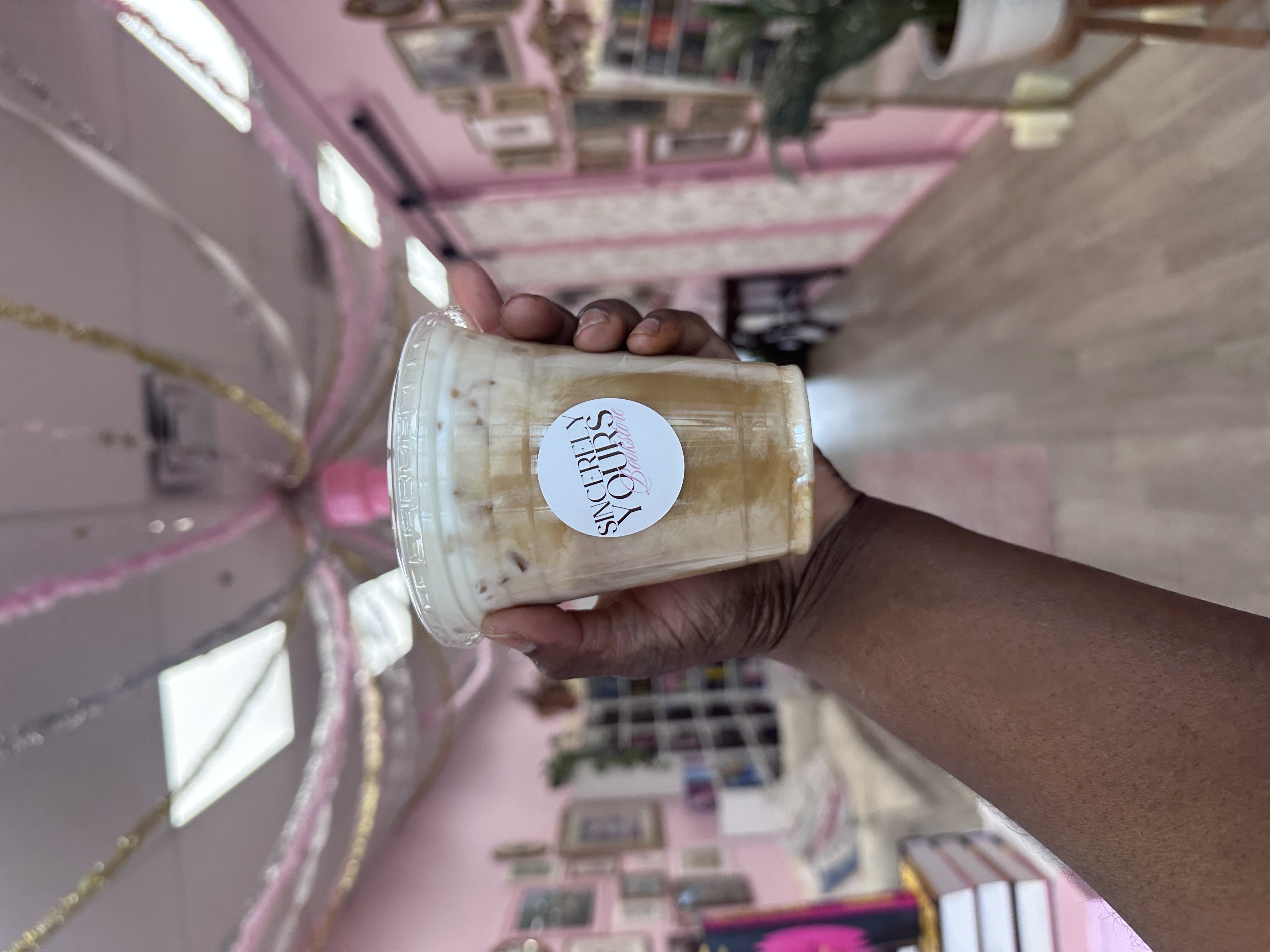 Tee Coffee Studio branded iced latte held up inside Sincerely Yours Bookstore Atlanta community event