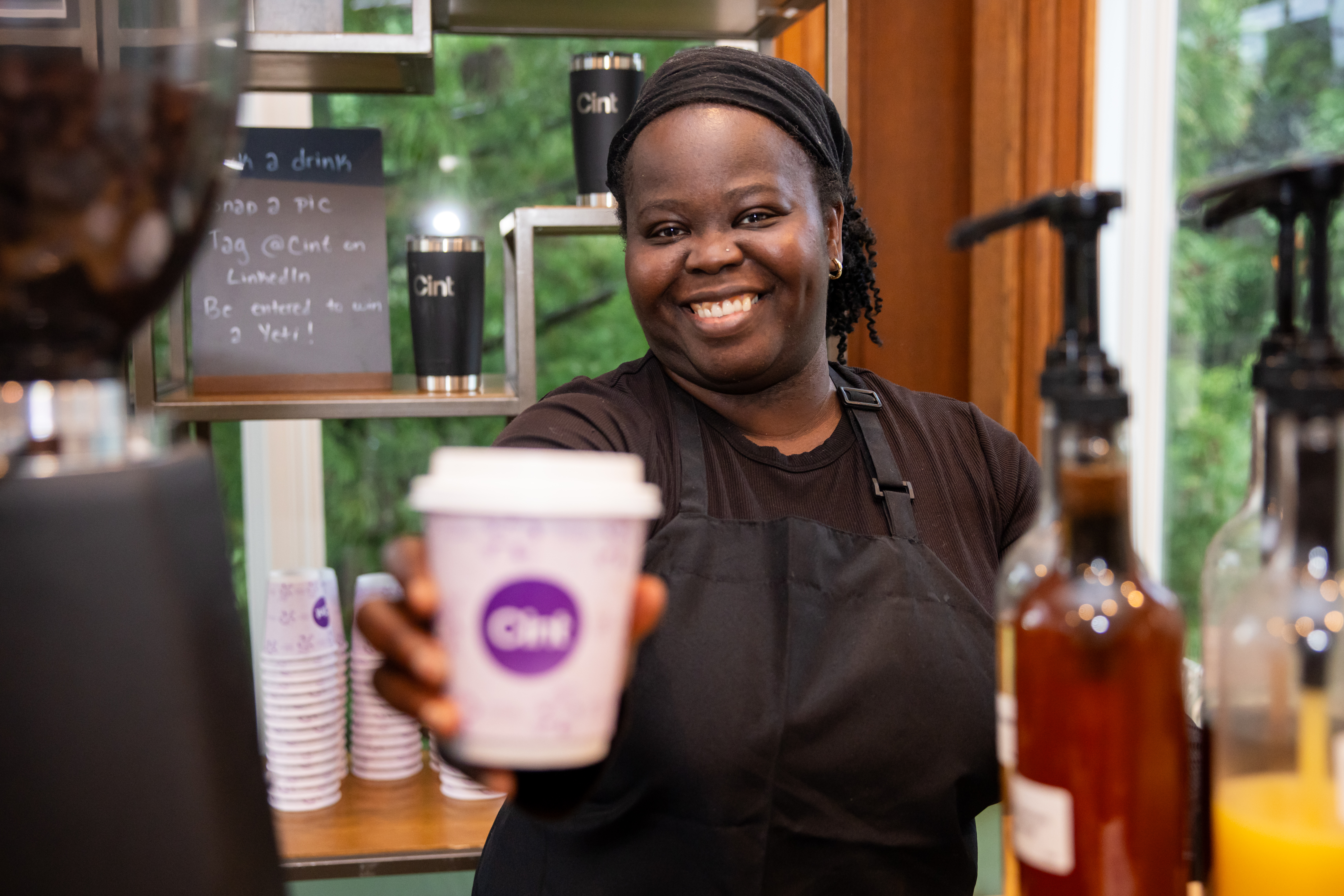 Tee George, founder of Tee Coffee Studio, extending a branded coffee cup toward a guest at an Atlanta corporate event — the moment of connection
