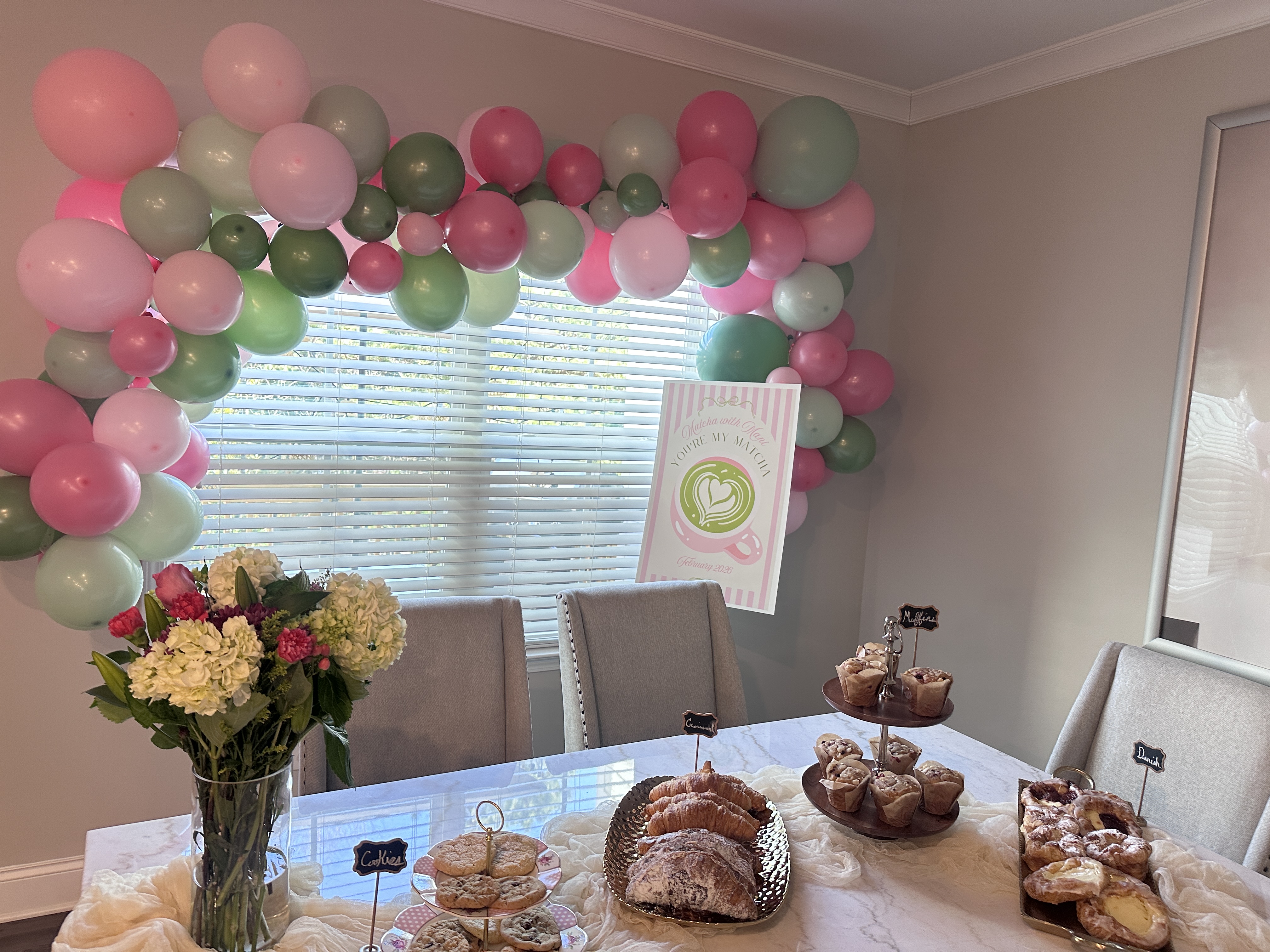 Pastry spread with croissants muffins and danish on display table with pink and green balloon arch