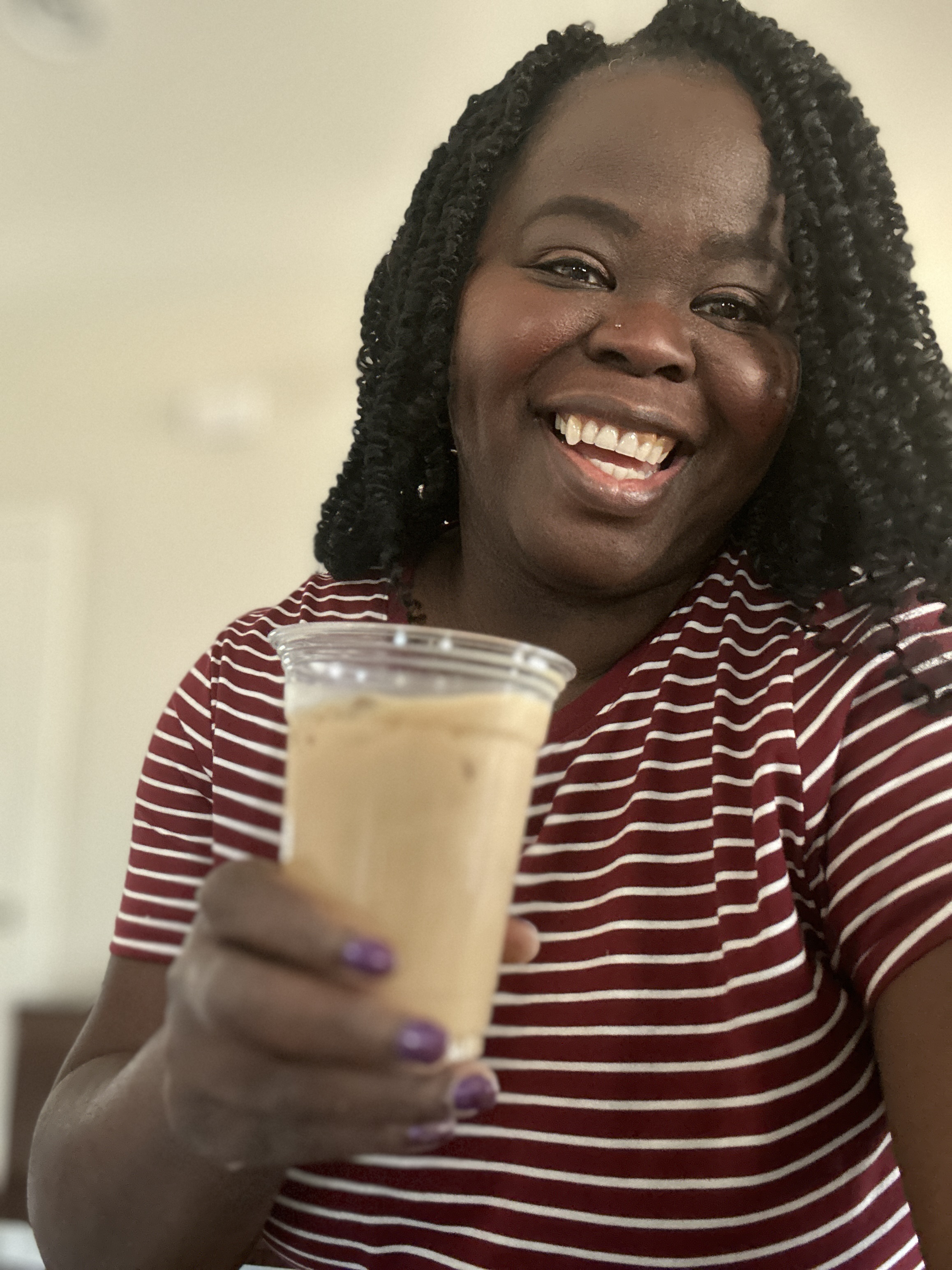 Tee George smiling and extending iced latte toward camera at Atlanta private celebration event